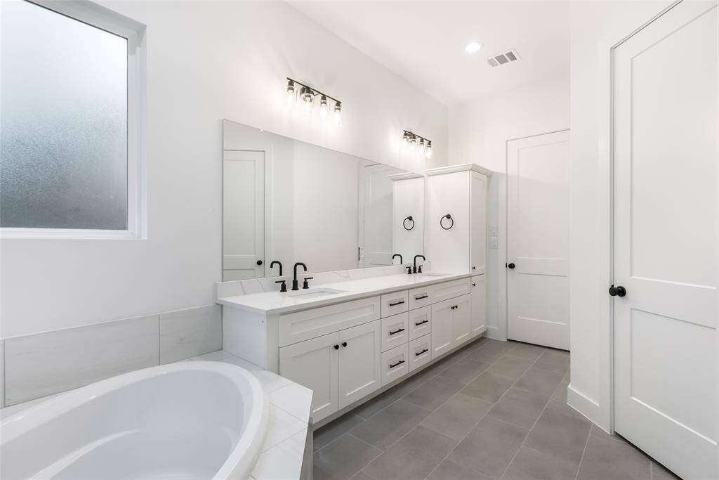 This bathroom features a clean and sleek vanity with black fixtures, and a large mirror. Natural light streams in through the window, highlighting the elegant marble-style flooring.