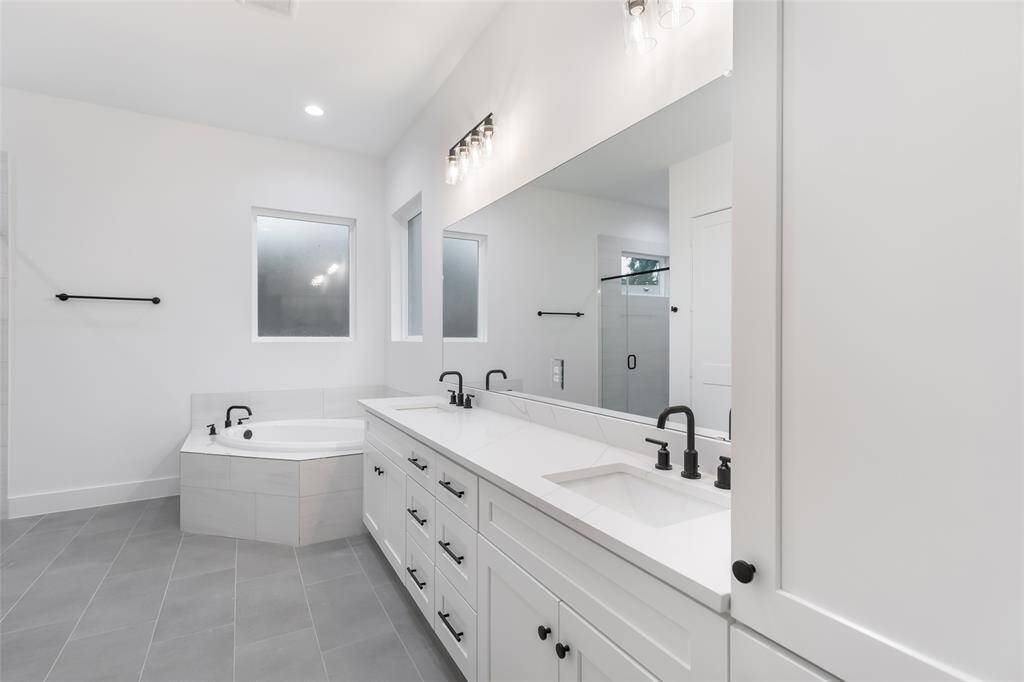 This bathroom features a modern design with a sleek dark vanity, gold fixtures, and a large mirror. The white walls and lighting create a bright, clean look.