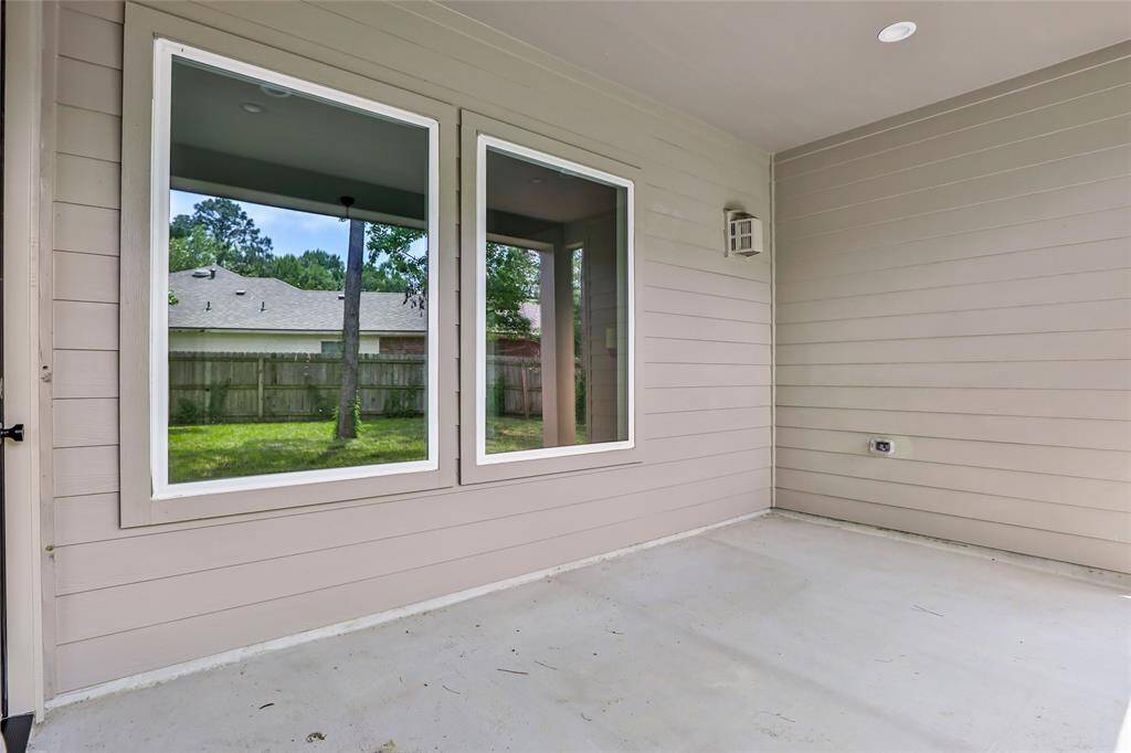 This photo showcases a covered patio with light-colored siding and two large windows, providing a view of the backyard with a wooden fence and trees. The space is clean and ideal for outdoor relaxation.