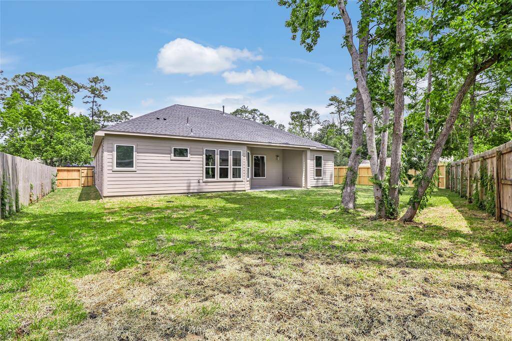 This photo showcases a spacious backyard with a well-maintained lawn and mature trees, providing a serene outdoor space. The house features a modern exterior with large windows and a covered patio, perfect for relaxation or entertaining. The yard is enclosed by a wooden fence, offering privacy and security.