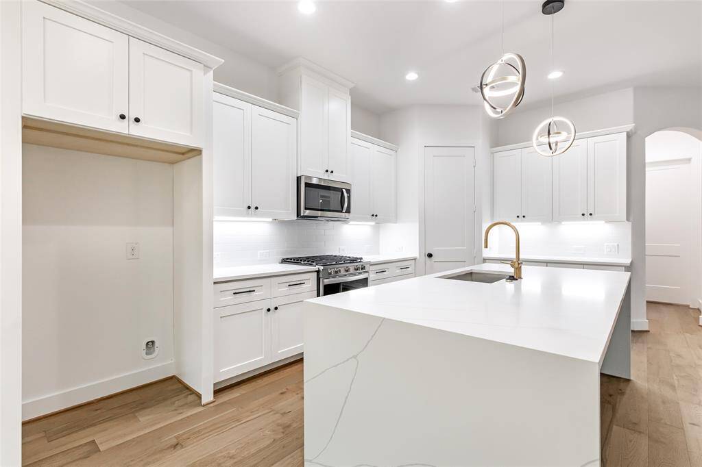 This modern kitchen features sleek water fall quartz, a spacious island and contemporary pendant lighting. It includes stainless steel appliances, a built-in microwave, and a stylish gold faucet, all set against a backdrop of light wood flooring.