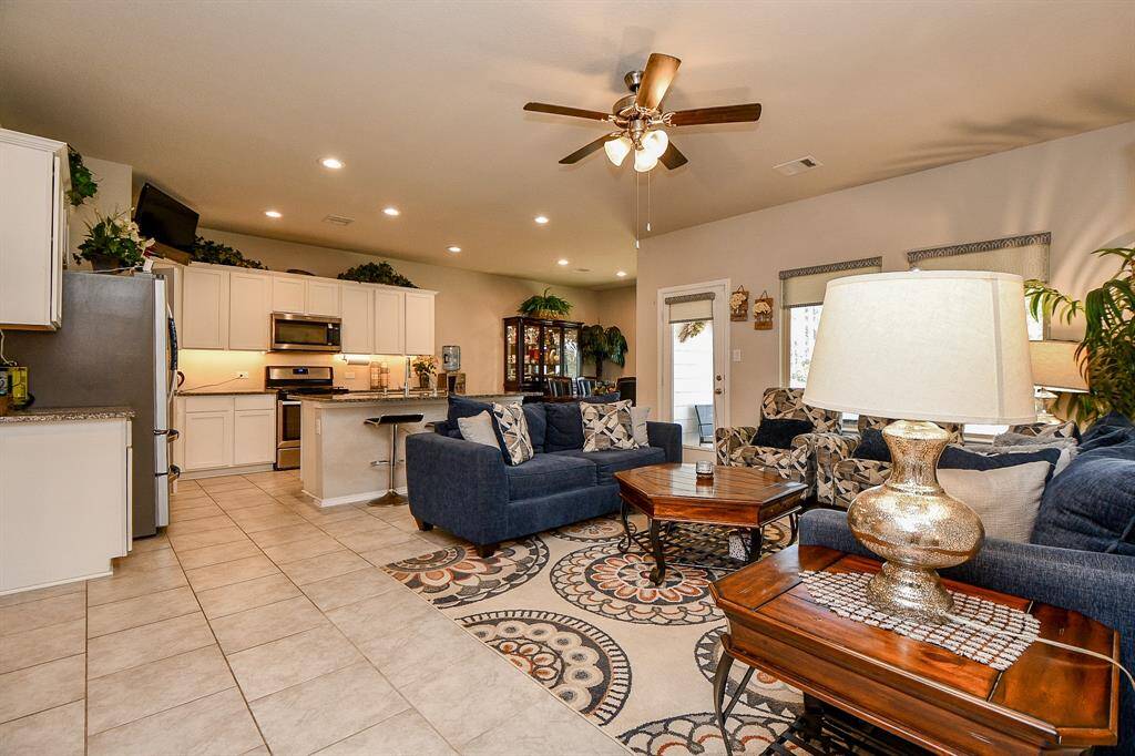 This open-concept living space features a modern kitchen with white cabinetry and stainless steel appliances, seamlessly flowing into a cozy living area. The room is adorned with stylish furnishings, decorative accents, and ample lighting.
