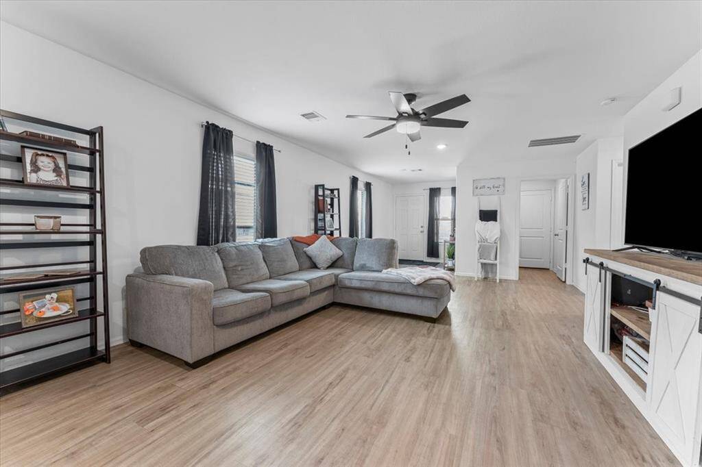 Spacious living room with a modern design wood-like vinyl flooring, ceiling fan, and ample natural light from multiple windows.