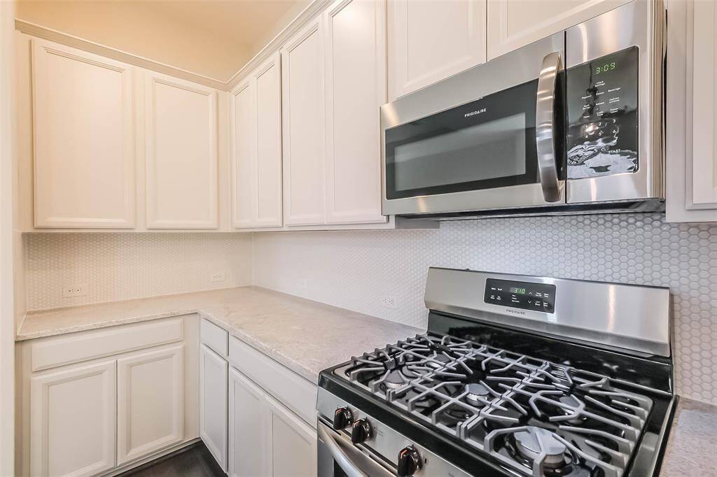 Another view of the kitchen features stone countertops, gas range, and beautifully detailed tile backsplash.