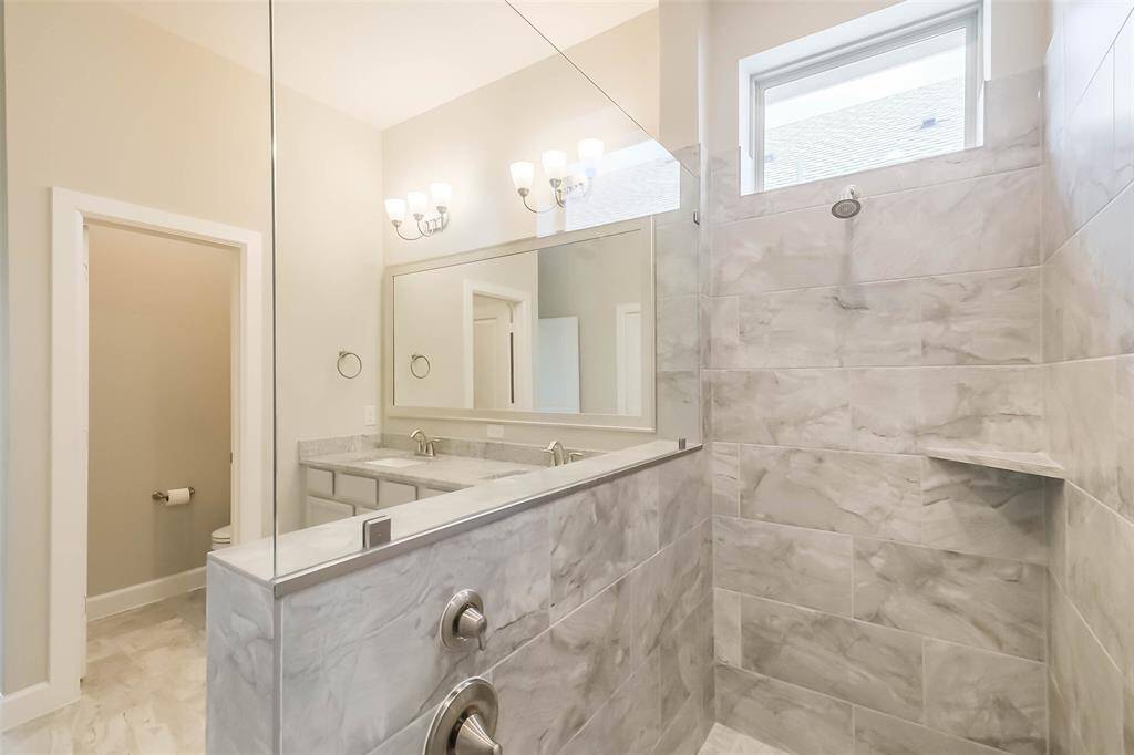 Another view of the primary bath with crisp clean lines and tile work, and water closet doorway on the left.