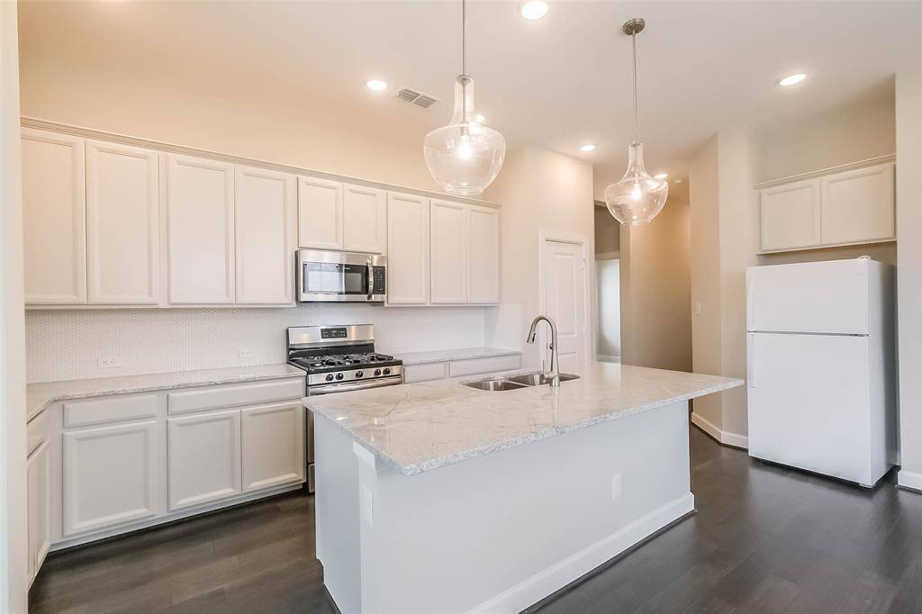 Another view of the kitchen features pendant lighting, stainless oven and microwave, high ceilings, and island with bar seating for entertaining.