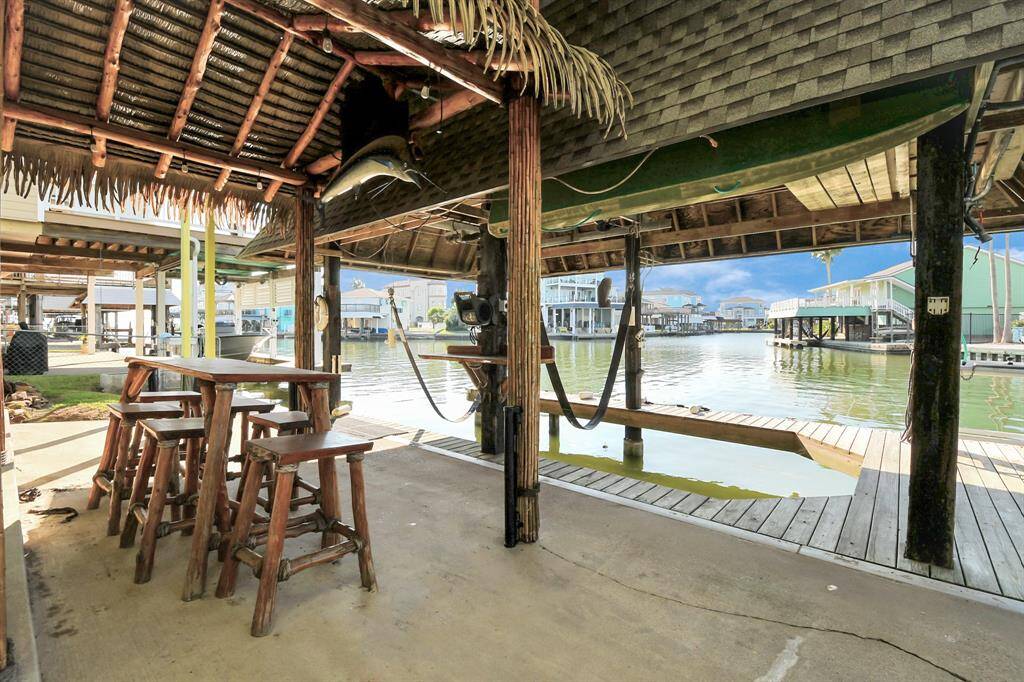 Charming waterfront patio with a rustic wooden bar setup under a thatched roof. Offers direct access to the water with a boat dock, perfect for relaxing and entertaining by the canal.