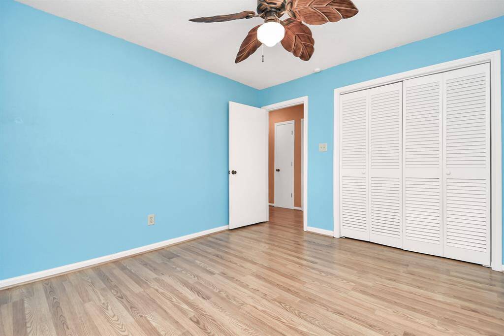 Bright and airy bedroom featuring vibrant blue walls, elegant wood flooring, and ample closet space with charming louvered doors. A stylish ceiling fan adds a touch of sophistication.