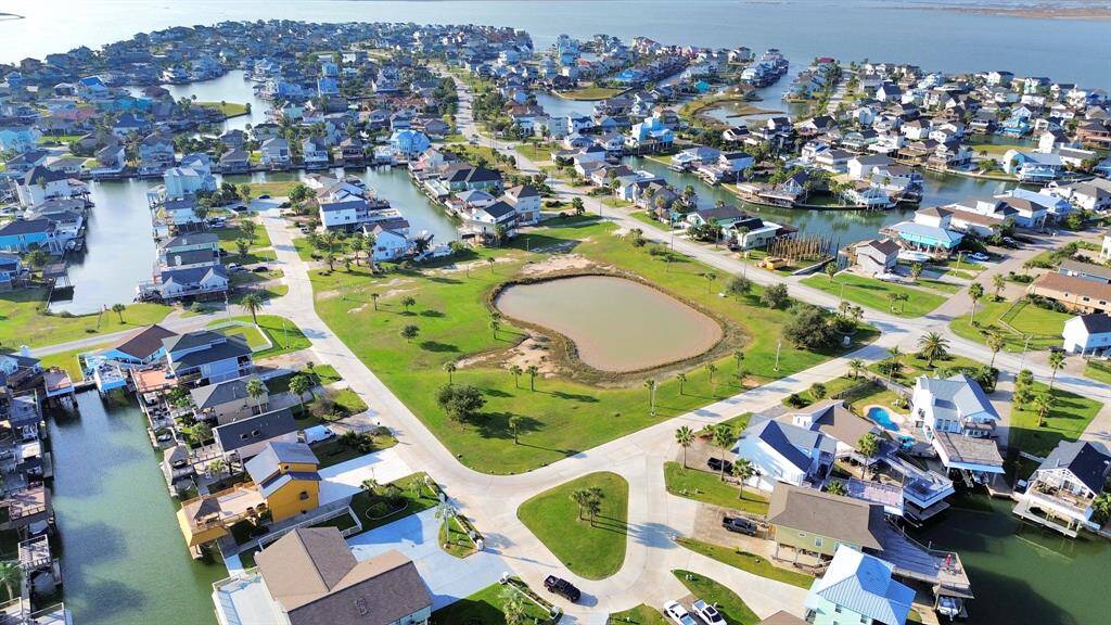 This aerial photo showcases a picturesque waterfront community with numerous homes lining canals and a central pond. The neighborhood offers scenic water views and lush greenery, ideal for those seeking a serene coastal lifestyle.