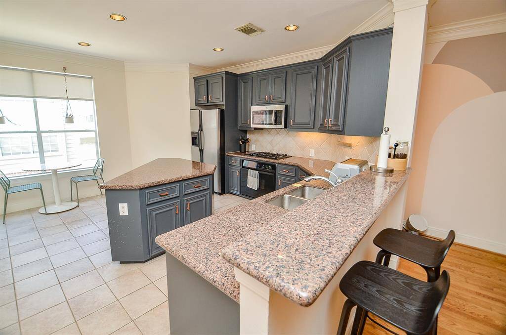 Tons of cabinetry, up and down, in a muted colonial blue/grey tone, adds fun and sophistication to this truly workable kitchen, with open floor paths; granite counters everywhere you land and bright tile backsplash.