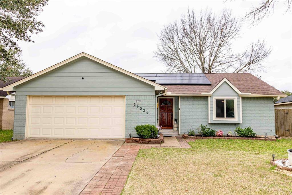This charming single-story home features a light green exterior. It has a two-car garage, a well-maintained front yard with a small garden, and a large tree providing shade. The property offers a welcoming entrance and is located in a quiet neighborhood.