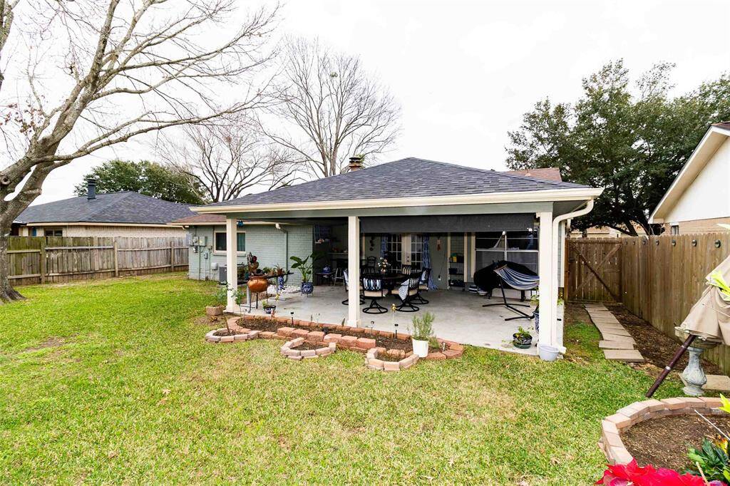 This image shows a cozy backyard with a covered patio area. The space is surrounded by a wooden fence and includes a small garden area with potted plants, making it ideal for relaxation and entertaining.
