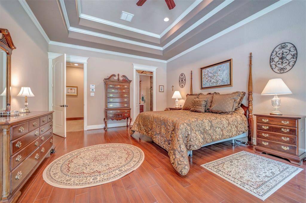 This Spacious Primary bedroom suite boasts the Tray Ceiling Feature with Stacked Moldings and Lighting, Picture windows and Entrance door to the Pool/Spa area, Wood flooring