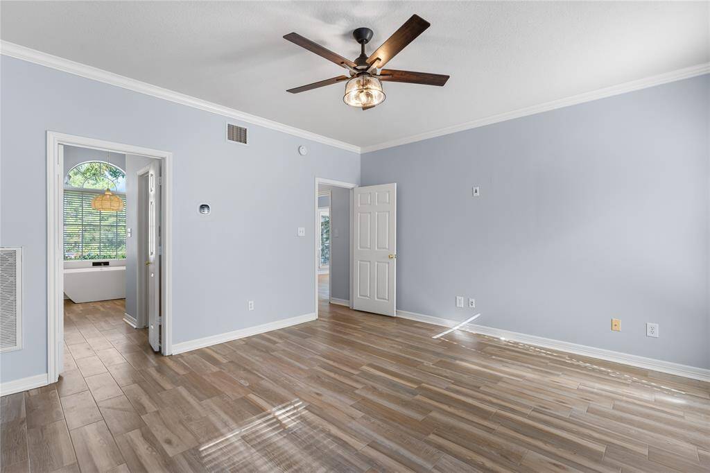 Primary bedroom downstairs with split floor plan, wood floors, recent paint, crown molding, ceiling fan and tons of light!