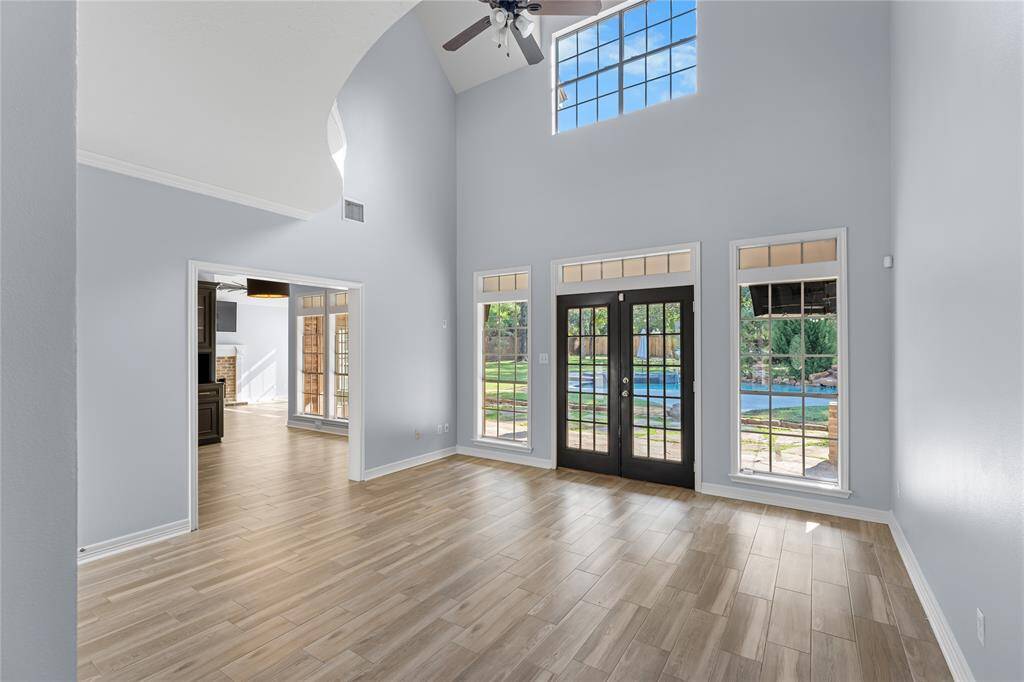 Formal living with high vaulted ceilings, large windows, wood floors and French doors leading to backyard and pool area.