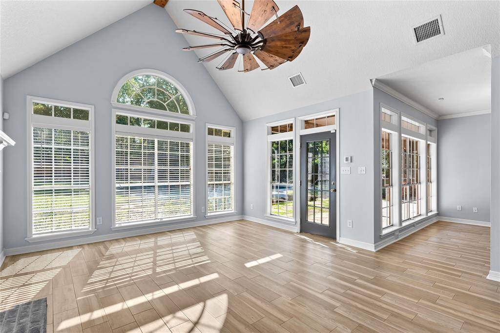 Den features high vaulted ceilings, large arched windows providing abundant natural light, and access leading to the outside. The wood floors add warmth to the fresh, airy feel of the space.