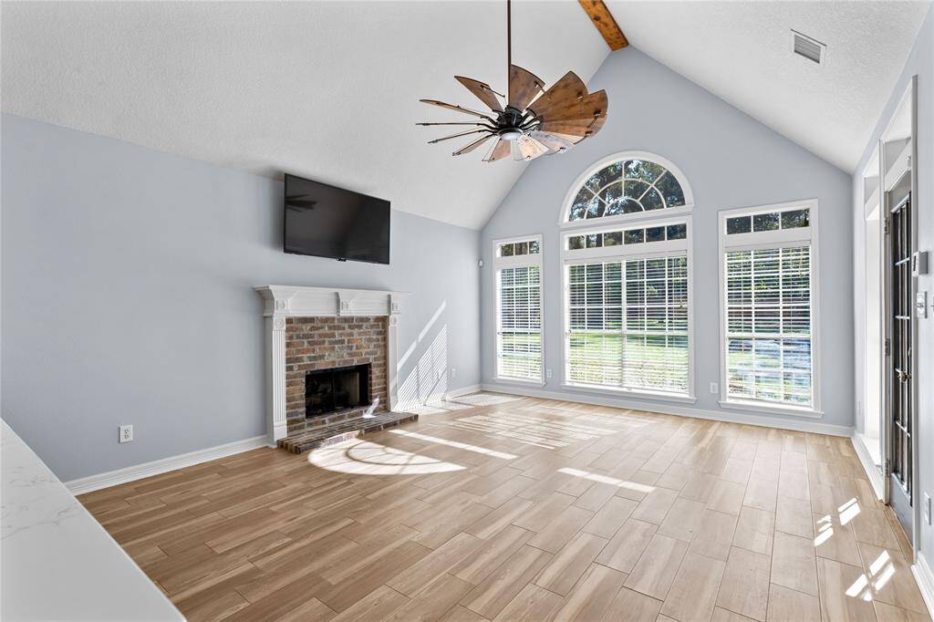 The den offers a bright and airy feel with a classic brick fireplace, and elegant wood flooring. A unique ceiling fan adds character to the space.