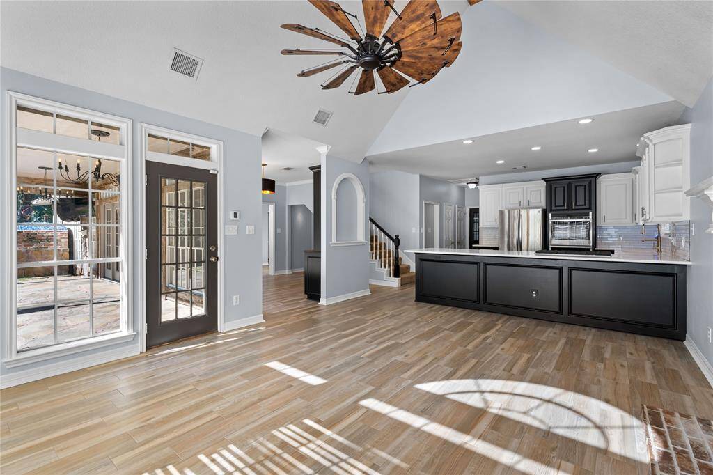 Another view of the den looking towards the open-plan kitchen with modern appliances, ample cabinet space, and a large island. Natural light floods in from the backyard leading to an outdoor area.