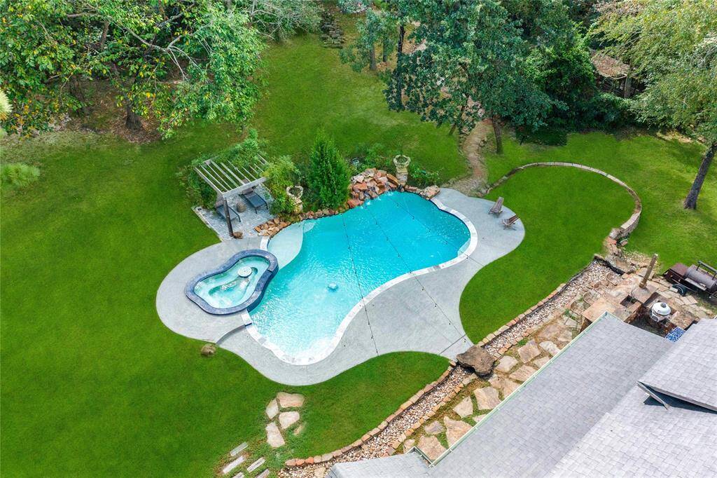 Spacious backyard with an inviting in-ground swimming pool and hot tub, surrounded by a well-maintained lawn with mature trees and a cozy patio area, perfect for outdoor relaxation and entertainment.