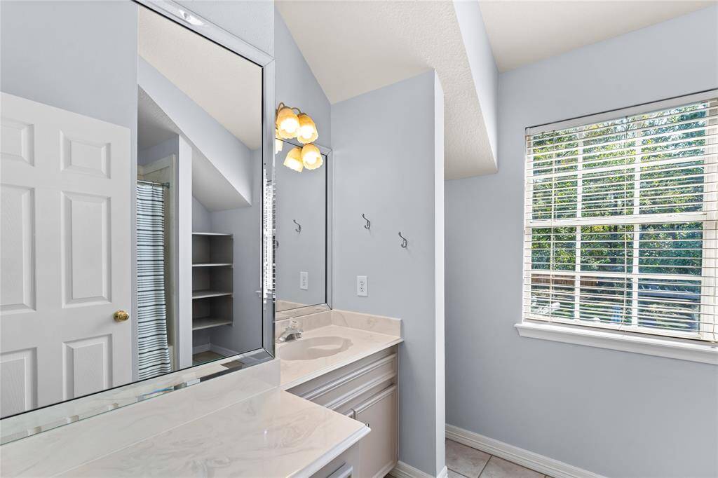 Secondary bathroom upstairs with modern finishes, featuring a large mirror, vanity area, ample storage space, and a window that provides natural light and a view of the backyard.