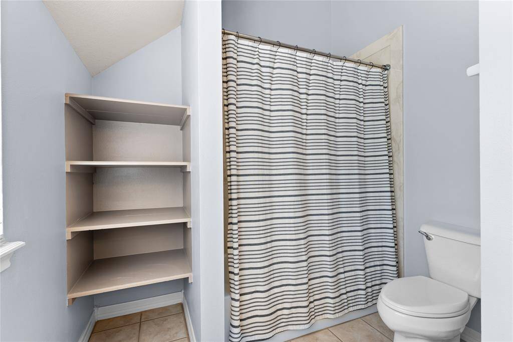 Secondary bathroom upstairs with a built-in shelving for storage & tub with shower.