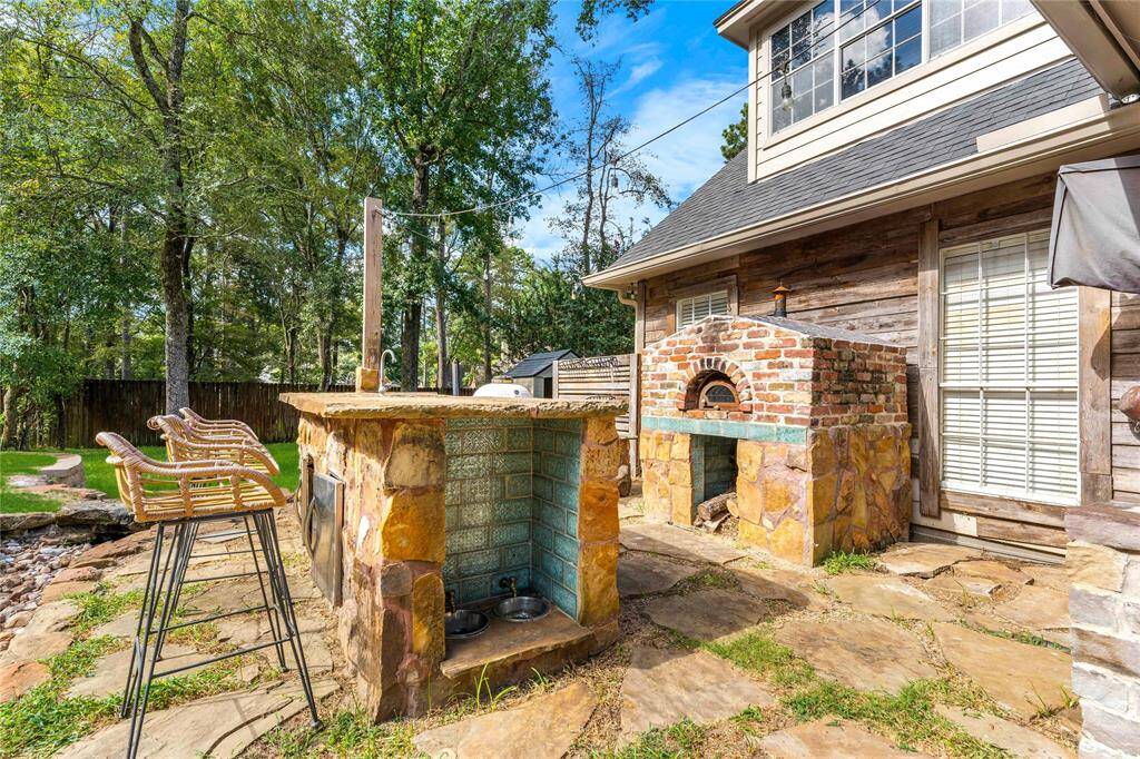 This outdoor space features a charming stone pizza oven and bar area, ideal for entertaining, set against a backdrop of mature trees providing a serene, private setting.  The dogs even have their own station for food and water bowls!