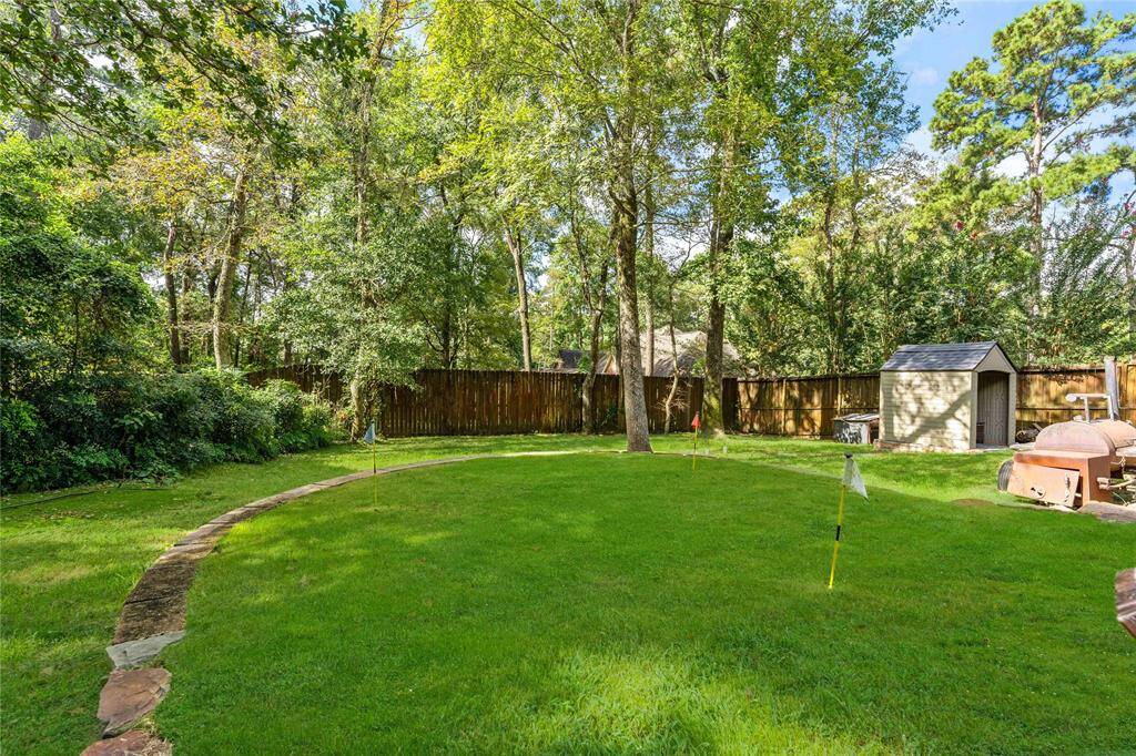 Lush green grass, mature trees, and a stone pathway. A wooden fence surrounds the perimeter for privacy, and a storage shed is visible in the background, offering additional utility space.