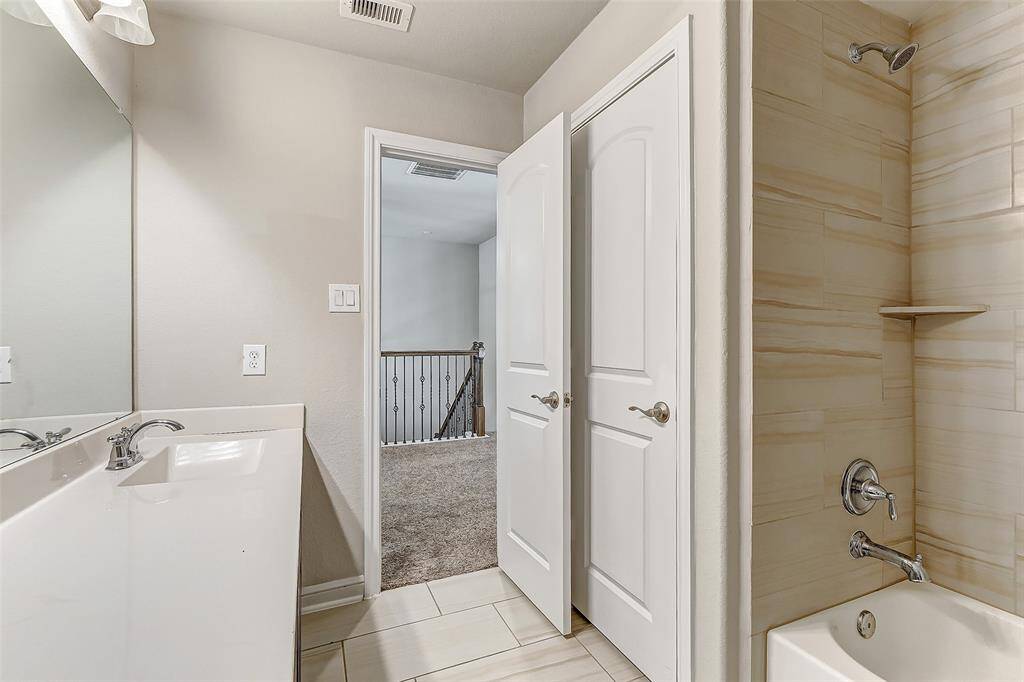 This guest bathroom offers a serene escape, with a sleek combination of tile and warm tones. The spacious shower-tub combo provides versatility for guests or family, while the ample vanity and lighting create a practical yet calming atmosphere. The clean design and modern fixtures make it a timeless addition to the home.