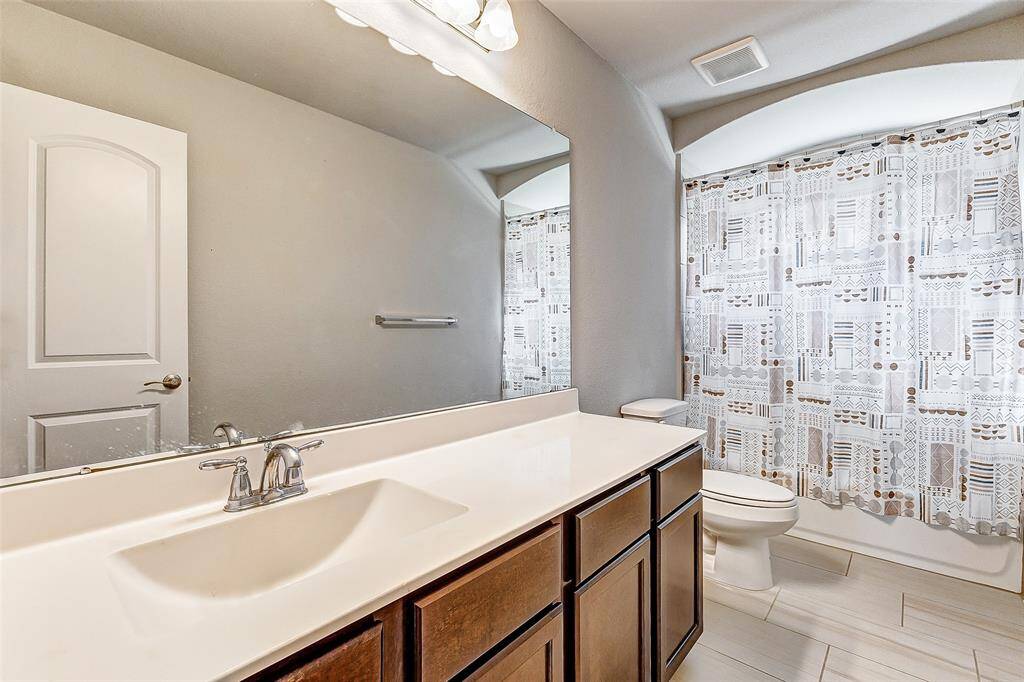A full bathroom featuring an elegant vanity with a wide countertop and ample storage underneath. The contemporary lighting fixtures and large mirror enhance the room's brightness, while the clean, tiled shower-tub combination ensures functionality with a touch of modern style.
