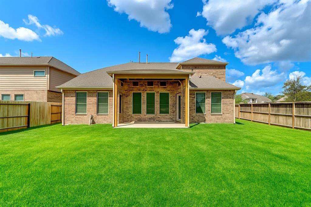 The rear view of the home showcases the elegant brickwork and spacious covered patio area. Large windows allow for ample natural light inside, while the well-maintained yard provides a serene, private oasis for family gatherings or quiet evenings.