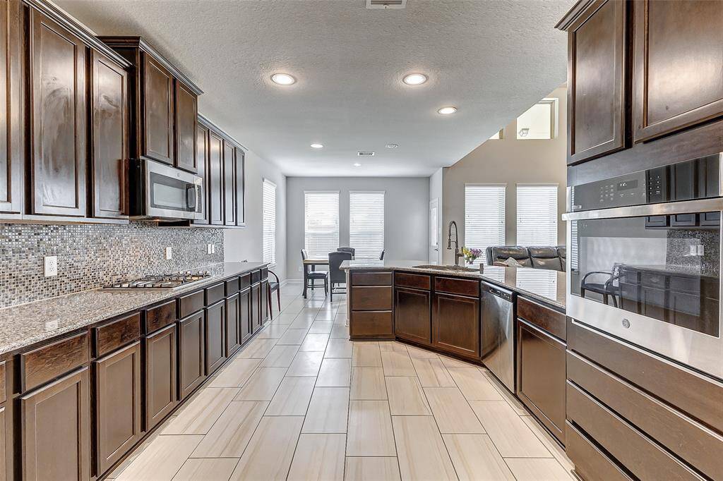Experience culinary bliss in this spacious, fully equipped kitchen, boasting sleek granite countertops, high-end stainless steel appliances, and a mosaic tile backsplash that adds a touch of elegance. The expansive layout offers ample cabinet storage and a convenient island for meal prep or gathering with family and friends. The open flow to the dining area makes entertaining seamless, with large windows filling the space with natural light.