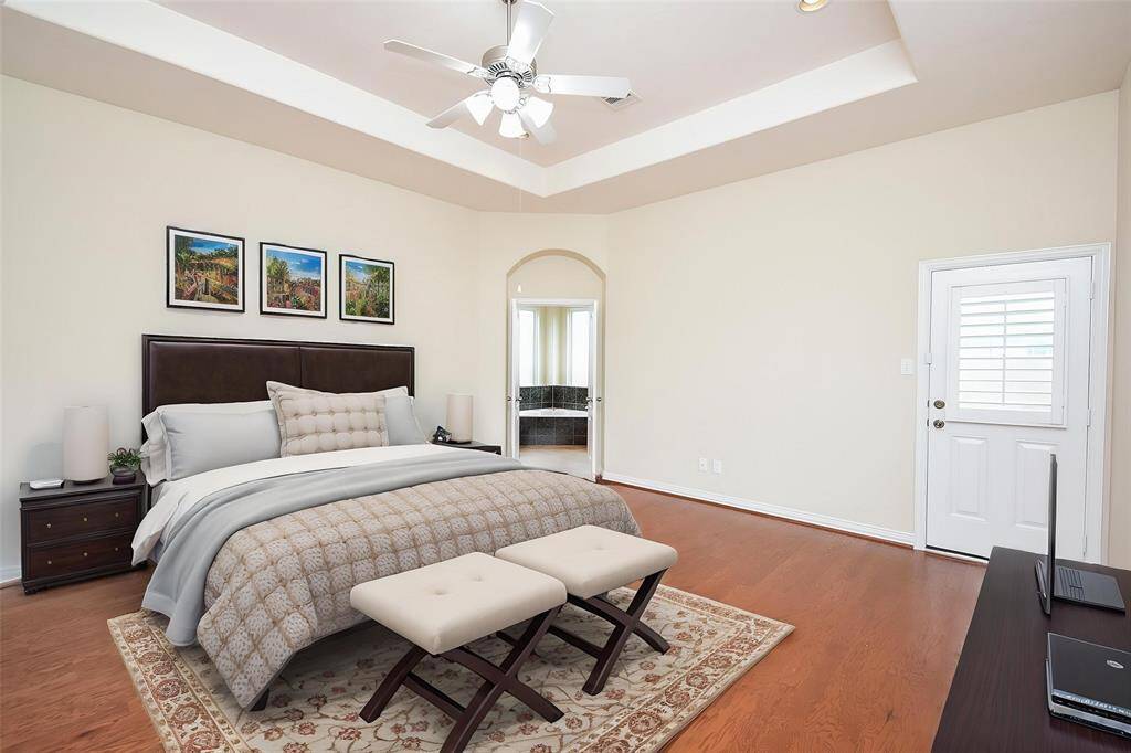 Large Primary Bedroom with tray ceiling, wood flooring, private door going to back yard and double doors leading into the large Primary Bathroom.