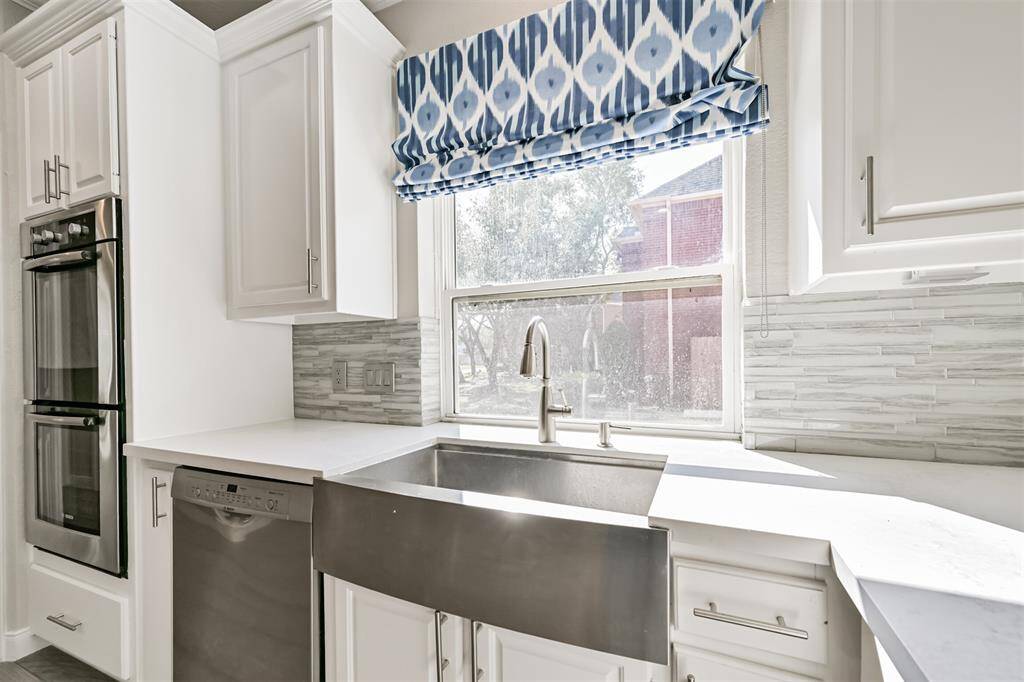 STAINLESS FARMHOUSE SINKWITH A PICTURE WINDOWOVERLOOKING THE BEAUTIFULBACKYARD.