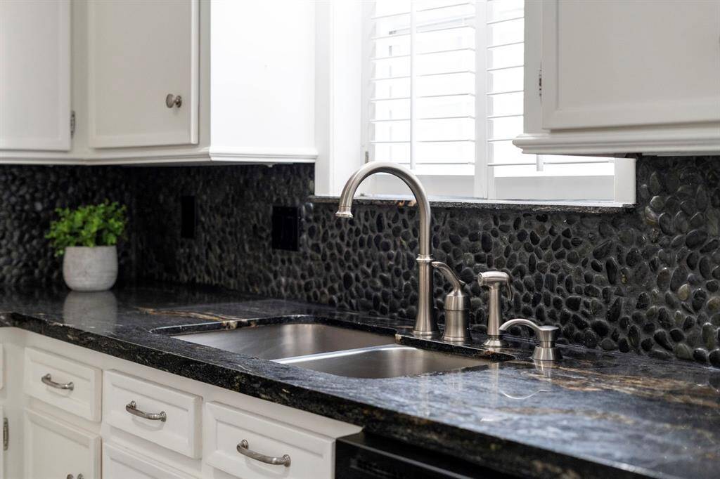 The kitchen has a stainless steel sink, pebble backsplash, and window with plantation shutters.
