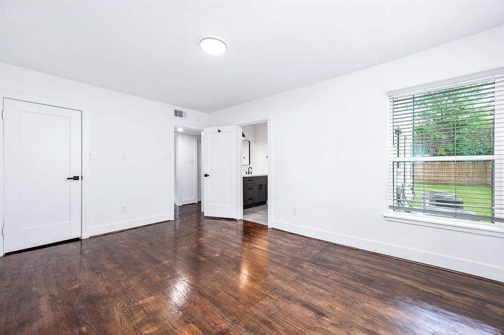 Freshly painted primary bedroom featuring rich hardwood floors and plenty of natural light through large windows.