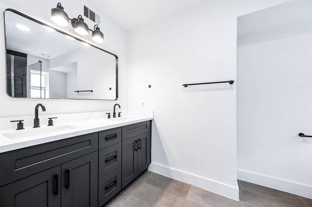 The primary bathroom features a modern double vanity with dark cabinetry, a sleek white countertop, stylish black fixtures, and a large framed mirror with overhead lighting