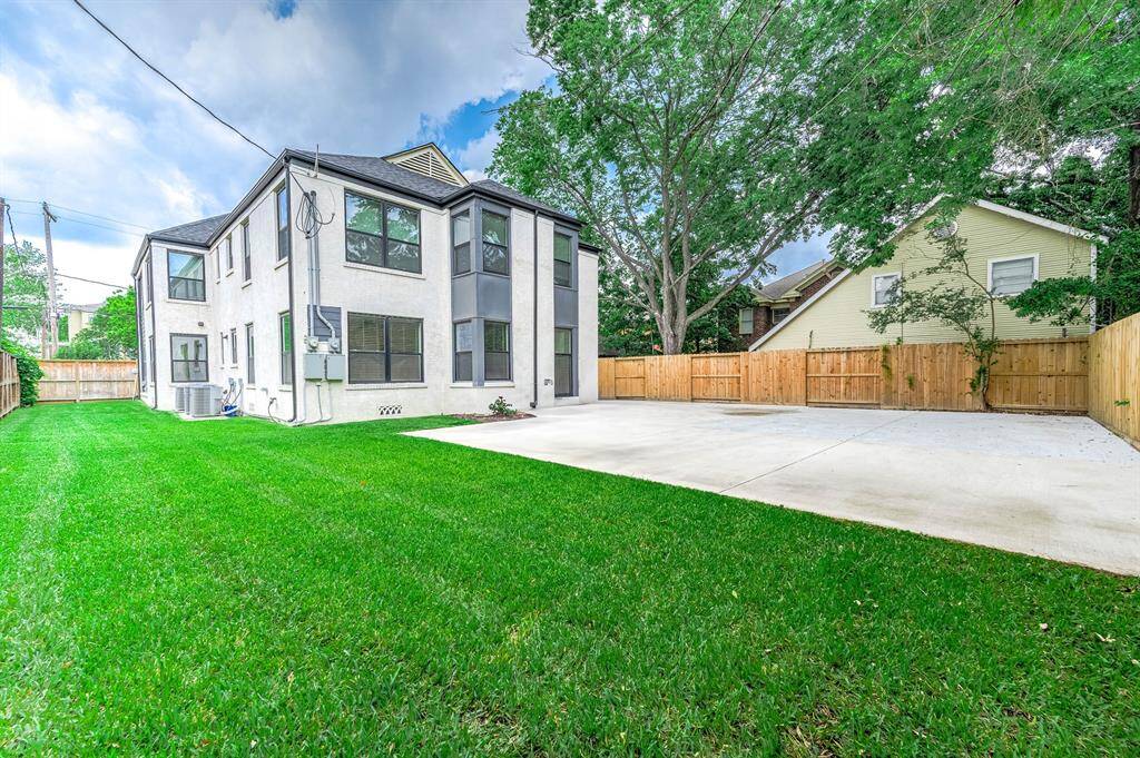 Spacious backyard featuring a well-kept lawn, a large concrete driveway, and mature trees offering plenty of shade. The fenced yard provides privacy, while modern windows add a fresh, contemporary look to the home's exterior.