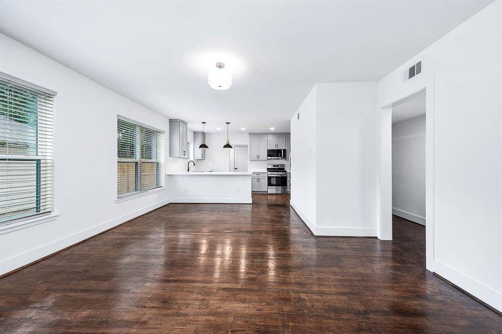 Bright and open dining area with polished hardwood floors, fresh white walls, and large windows with blinds. An open doorway to the living room enhances the home's open-concept feel.