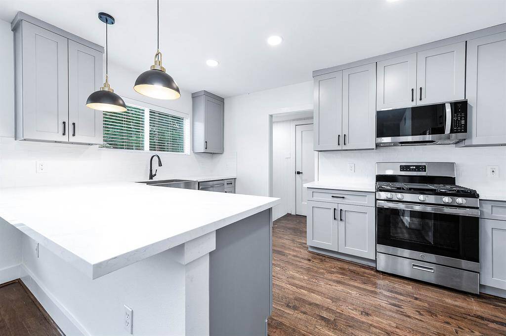 This kitchen showcases brand-new modern gray cabinetry, new stainless steel appliances, a sleek white island, and original hardwood floors, blending style and functionality in one inviting space.