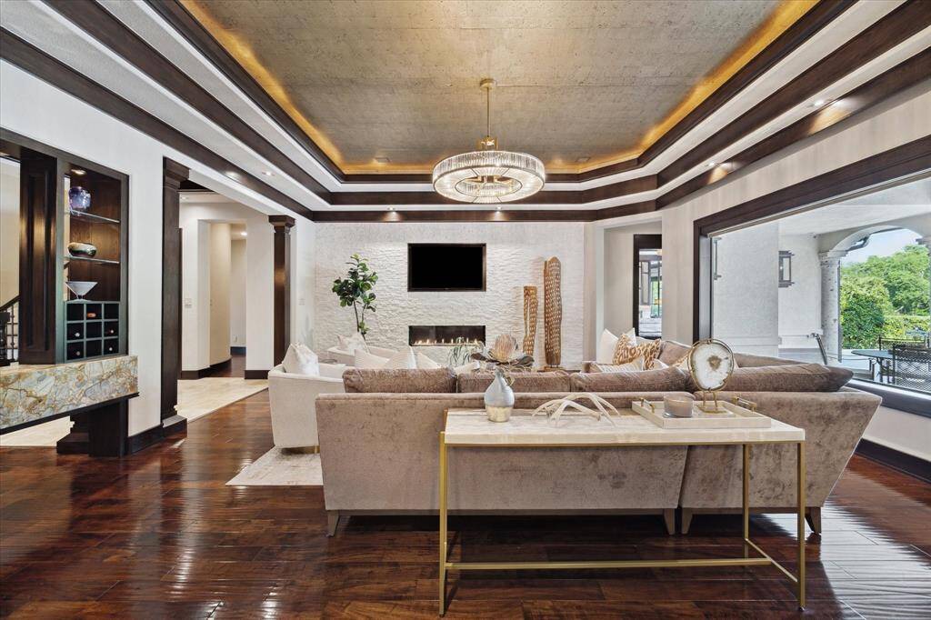 This welcoming living room is perfectly tailored for entertaining. From this vantage point, the imported Onyx serving bar—ideally positioned between the living and formal dining rooms—offers easy access for serving cocktails during gatherings. The open-concept layout encourages effortless flow into surrounding spaces, while the expansive picture windows highlight the covered patio and lush landscape, beautifully merging indoor comfort with outdoor charm.