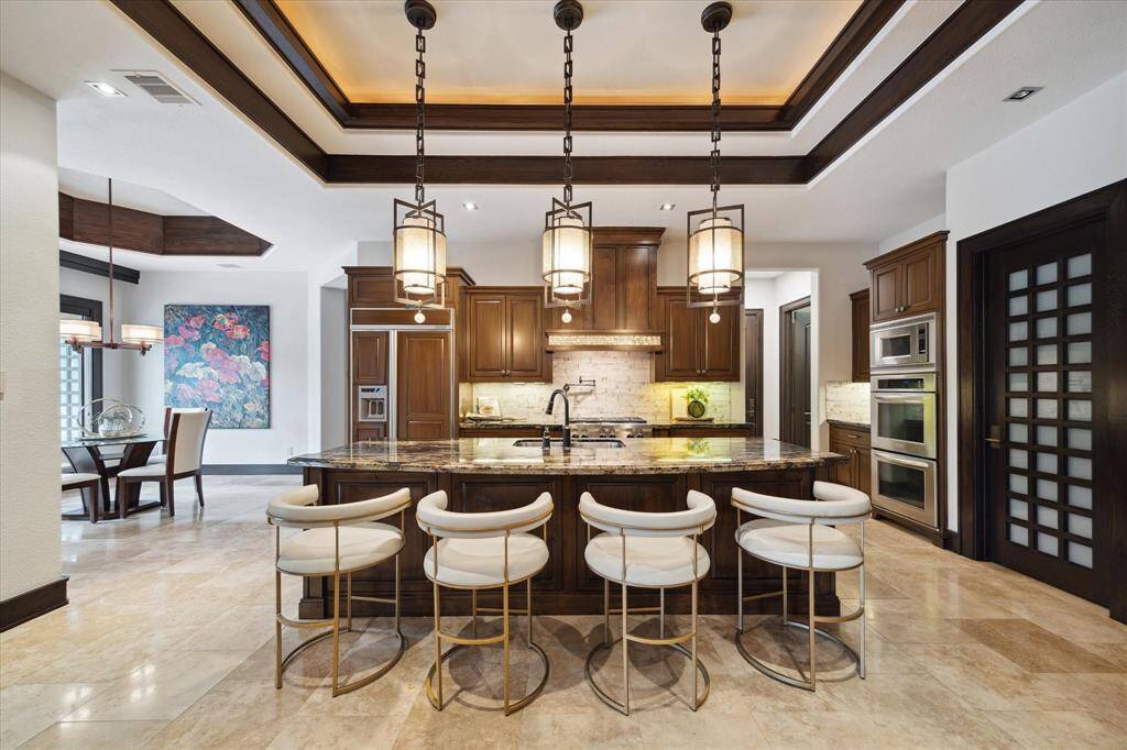 This chef-inspired kitchen combines warmth and sophistication with custom wood soft-close cabinetry, professional-grade appliances, and an exotic granite island that seats four. The trio of designer pendant lighting, tray ceiling with cove accents, and built-in dual convection ovens with microwave elevate both form and function. A custom paneled refrigerator and prep sink enhance everyday usability, while the adjacent breakfast area and open layout make this space ideal for casual mornings.