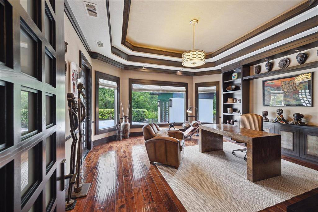 This richly appointed study features custom millwork, patio door, tray ceilings with layered wood molding, and hand scraped wood flooring that adds timeless elegance. A wall of windows frames peaceful pool and garden views, filling the space with natural light and creating an inspiring environment for productivity or relaxation. Built-in shelving and display cabinetry offer both style and function, which also provides a perfect setting for using this space as a first-floor game room.