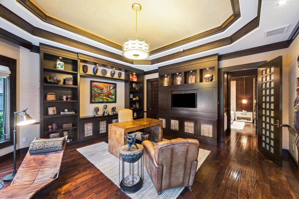 This alternate view of the sophisticated 18’ x 18’ home office highlights richly stained custom built-ins with integrated accent lighting, a media-ready display wall, and a generously sized walk-in closet through the 8-foot custom wood and milk glass door. With direct access to the adjacent bedroom, the space is thoughtfully designed for productivity or relaxing in peace. A perfect balance of function and refinement, it adapts effortlessly, making this space truly versatile.