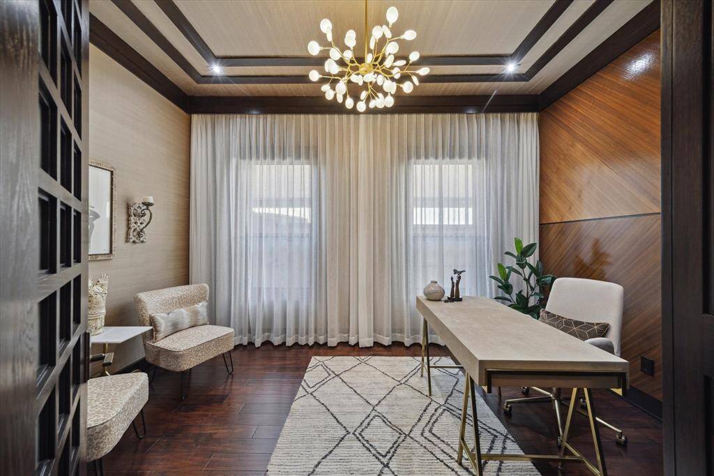 This stylish secondary office offers a refined and tranquil setting, featuring a dramatic contemporary chandelier, wood-trimmed tray ceiling with inlaid lighting, imported European silk wall coverings, and richly toned hardwood flooring. Soft sheers filter natural light through double windows, while a sleek desk and chic seating area create a comfortable space for reading, working, or quiet reflection. A perfect blend of calm, class, and contemporary flair.