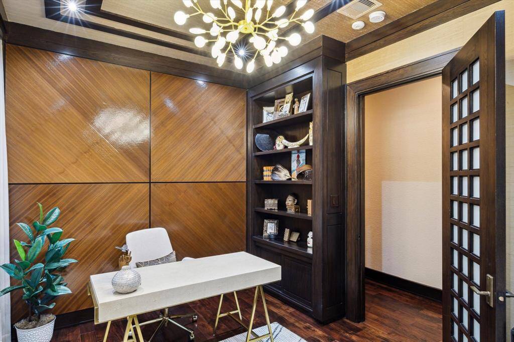 This additional angle of the secondary office showcases the room’s deeply grained wood-paneled feature wall and built-in display shelving, perfect for showcasing books, art, or personal mementos. The modern sculptural chandelier adds a modern touch of whimsy, while rich trim work and the 8-foot custom wood and milk glass door ground the space in warmth and sophistication. Whether used as a private study or reading room, this Zen-inspired space is as functional as it is visually impressive.