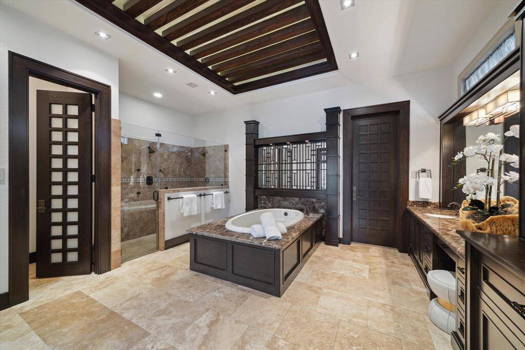 This tranquil primary bathroom includes an expansive glass-enclosed walk-in shower with multiple shower heads and built-in bench seating. A separate lavatory, tucked behind an 8-foot wood and opaque glass door, offers added privacy. Thoughtfully designed by famed Miami based designer, Adriana Hoyos, this ensuite retreat blends sophisticated style with resort-inspired comfort, creating a spa-like experience perfect for relaxation and daily indulgence.