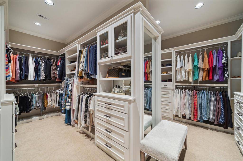 Styled to mimic a high-end Fendi boutique, this masterfully designed 18’ X 15’ walk-in closet is a dream for organization and style, featuring custom built-ins, glass-front cabinetry, and abundant hanging space. Thoughtfully arranged shelves and drawers provide dedicated storage for everything from accessories to seasonal wear, while a full-length mirror add functionality and elegance. A luxurious, boutique-inspired space tailored for daily ease.