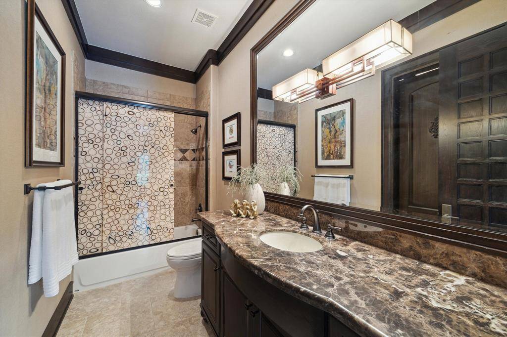 One of five guest bathrooms, this refined bathroom pairs warm tones with polished finishes, creating a stylish and welcoming atmosphere. A richly veined granite countertop adds a sense of luxury, while framed mirrors and contemporary lighting enhance the space’s elegance. The tub/shower combination features detailed tilework and a bold patterned glass enclosure, offering both function and flair. Ideal for guests, it delivers comfort with an upscale touch.