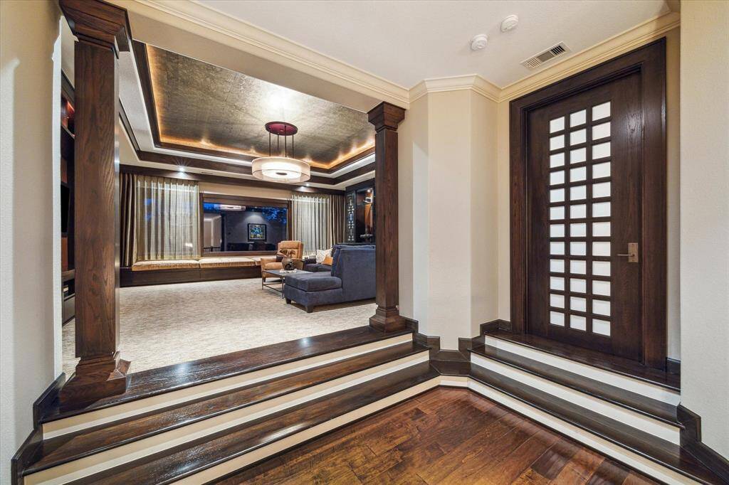A circular staircase topped by a magnificent rotunda ceiling with exquisite lighting leads up to this dramatic split-level entry to the second-floor game room and home gym.  Framed by richly stained wood columns and millwork, the rich tones are echoed in the game room’s tray ceiling, which features a gold leaf inset, cove lighting, and a contemporary chandelier that adds a touch of glam. The ambient light provided by the trio of windows and custom lighting creates an inviting atmosphere.
