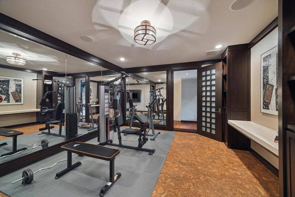 This well-appointed fitness room offers a motivating space to focus on health and wellness. Mirrored walls enhance the sense of openness and light, while sound dampening cork flooring ensures comfort and safety during training. Built-in shelving and a desk nook provide convenient storage and organization, and the adjacent flex room creates seamless access for post-workout relaxation. Through the custom built-in bookshelf, you’ll find a hidden room currently being used as an art studio.